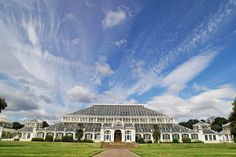 a large glass house sitting in the middle of a lush green field under a blue sky