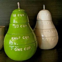 three ceramic pears sitting next to each other on top of a wooden table with cups