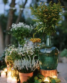 flowers and candles are sitting on a table in front of a vase with greenery