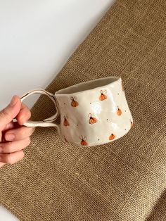 a hand holding a coffee cup on top of a brown cloth covered placemat with bees