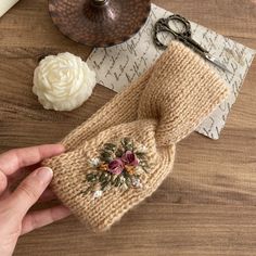 a hand is holding a knitted mitt with flowers on it next to a candle