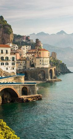 an old bridge over the water with buildings in the back ground and mountains in the background