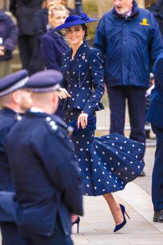 a woman in a blue dress and hat walking down the street with other people behind her