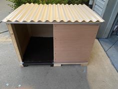 a dog house made out of plywood with a metal roof and door open on the sidewalk