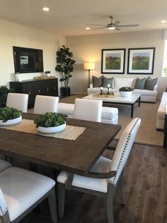 a dining room table with white chairs and a bowl of greens on top of it