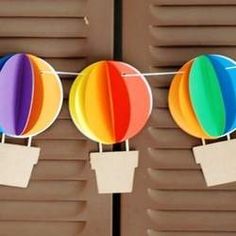 three colorful hot air balloons hanging from clothes pins with tags attached to them, in front of shutters