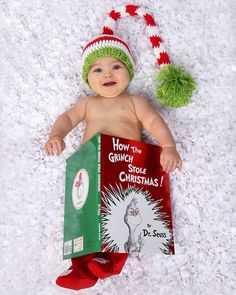 a baby wearing a green and red hat is laying on the ground with a book