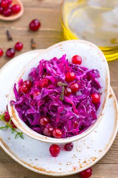 a white bowl filled with red cabbage and cranberries on top of a wooden table