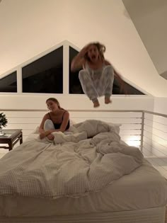 two women are sitting on a bed in a room with white walls and flooring