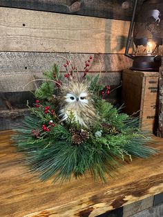 an owl sitting on top of a wooden table next to pine cones and red berries