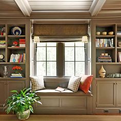 a window seat with bookshelves in front of it and a potted plant next to it