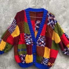 a multicolored cardigan sweater hanging on a hanger against a stone wall