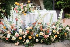 an arrangement of flowers on a table in the middle of a courtyard with wine glasses