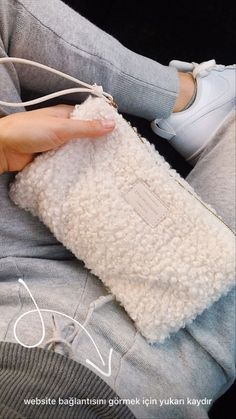 a woman is holding a white purse on her lap and wearing grey sweatpants while sitting down