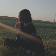 a woman sitting in the grass with flowers on her lap and sun shining behind her