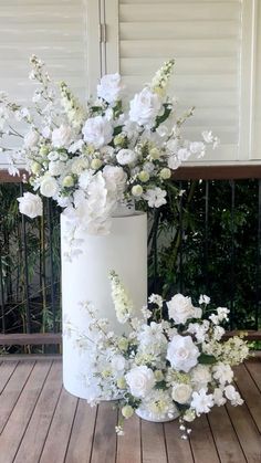 a white vase filled with flowers sitting on top of a wooden floor next to a fence