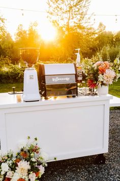 an outdoor bar with flowers on the side and a blender sitting on top of it