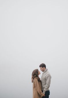 a man and woman standing next to each other on top of a hill in the fog