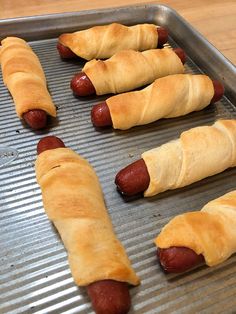 four hot dogs wrapped in croissants sitting on a pan with other sausages