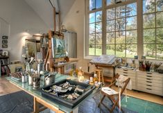 an artist's studio with lots of art supplies on the table and large windows