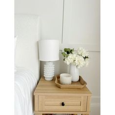 a white vase with flowers on a wooden table next to a bed