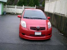 a red car parked in a parking lot next to a house and fenced in area