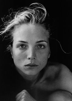 a black and white photo of a woman with her hair blowing in the wind, looking at the camera