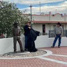 two men standing next to a statue on top of a brick road near a building