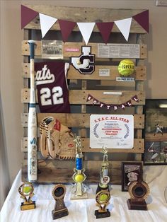 several trophies are displayed on a table in front of a wooden pallet with pennants