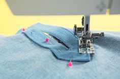 the sewing machine is working on the blue material that has been stitched together with pink pins