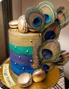 a multi - colored cake with peacock feathers on top and gold decorations around the edges