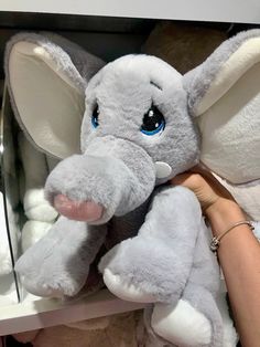 an elephant stuffed animal being held by a woman's hand in a store display case