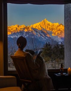 a person sitting in a chair looking out the window at snow covered mountains and trees