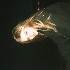 a woman with long hair standing in the dark looking at the camera while wearing a black jacket