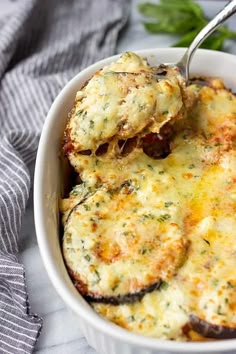 a white bowl filled with eggplant and cheese casserole next to a fork