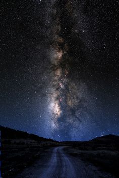 the milky shines brightly in the night sky above a dirt road and mountain range