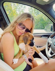 a woman sitting in the driver's seat of a car holding a small dog