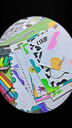 several different colored pencils and paper on top of a white circular plate with black background