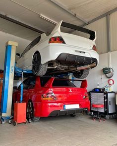 a white car is on top of a red car in a garage