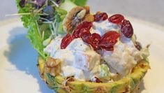 a pineapple topped with fruit and yogurt on a white plate next to lettuce