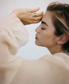 a close up of a person touching their forehead with one hand and wearing a ring on the other