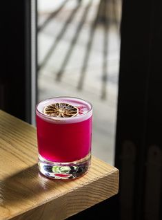 a glass filled with liquid sitting on top of a wooden table next to a window