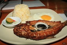 a white plate topped with meat, rice and an egg next to a knife and fork