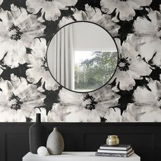 a black and white floral wallpaper with a round mirror on the side table in front of it