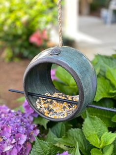 a bird feeder hanging from the side of a bush with purple flowers in the background