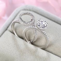 two wedding rings sitting on top of a white cloth with pink flowers in the background