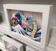 an art piece is displayed in a white frame on the wall above bookshelves