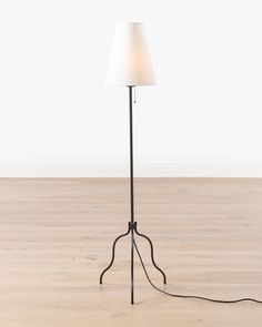 a floor lamp with a white shade on the top and an iron base, standing on a hard wood floor