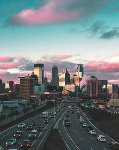 cars are driving down the highway with tall buildings in the background at sunset or dawn