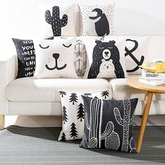 a white couch with black and white pillows sitting on it's side table next to a coffee table